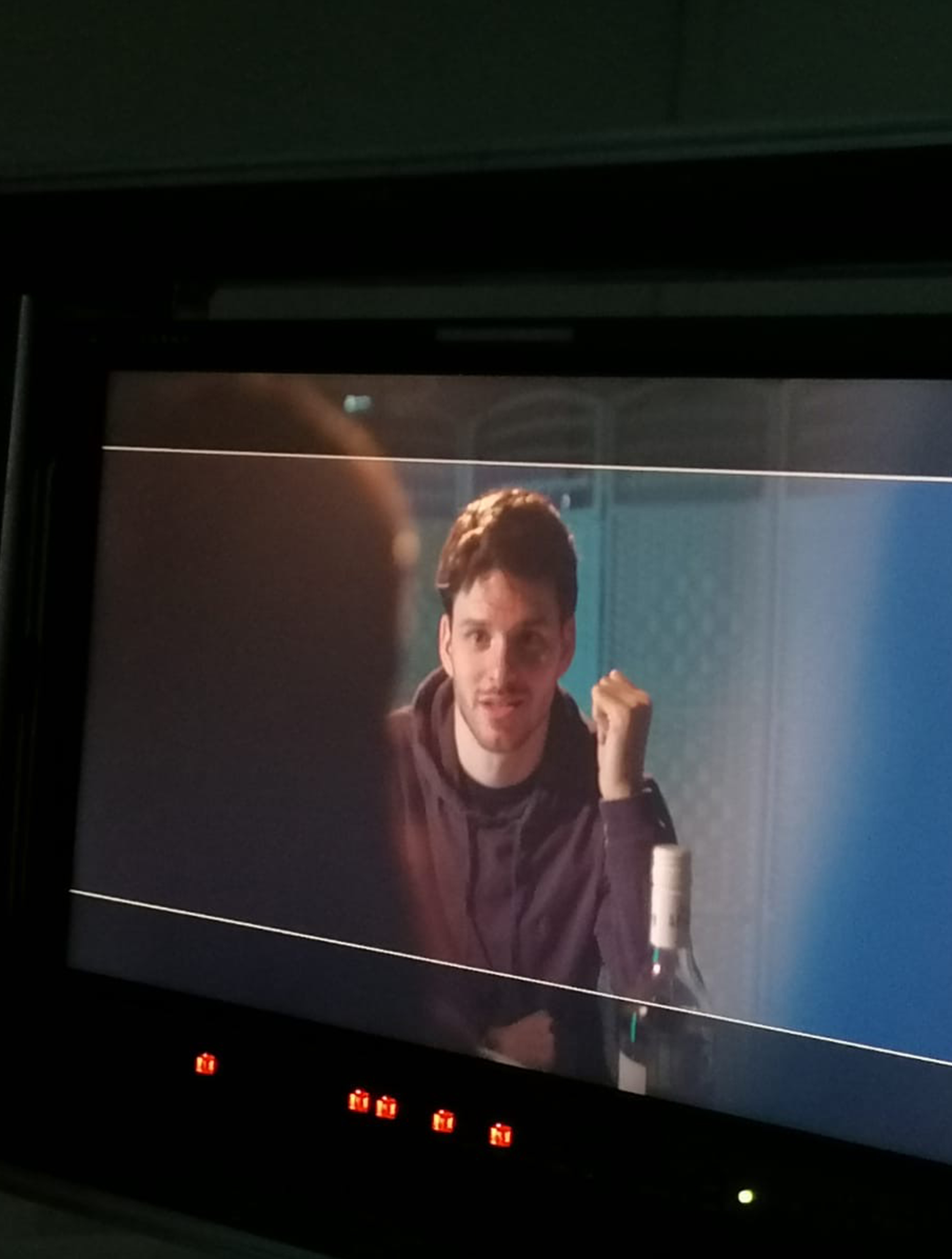 A video monitor showing Sam Hume on set wearing a hoody and sat next to a bottle of wine