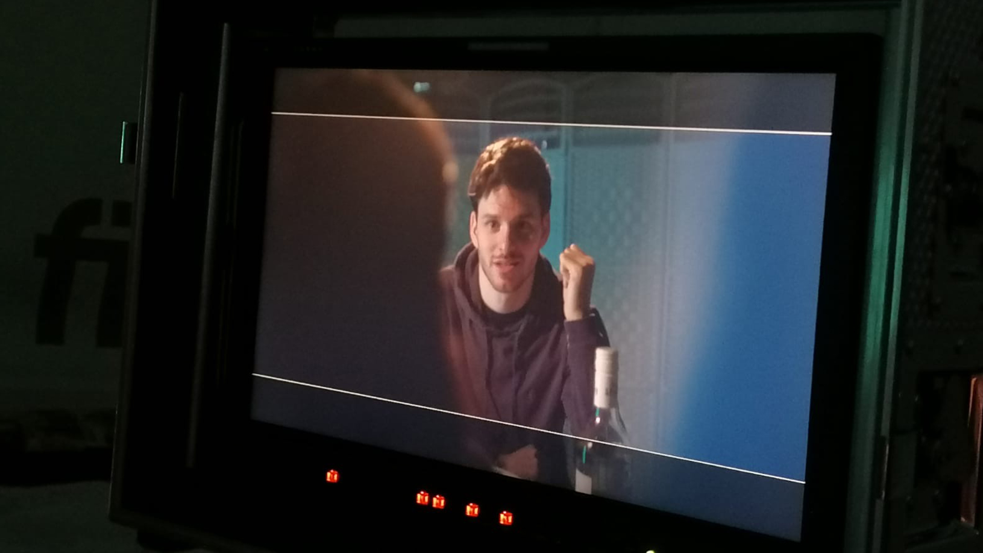 A video monitor showing Sam Hume on set wearing a hoody and sat next to a bottle of wine