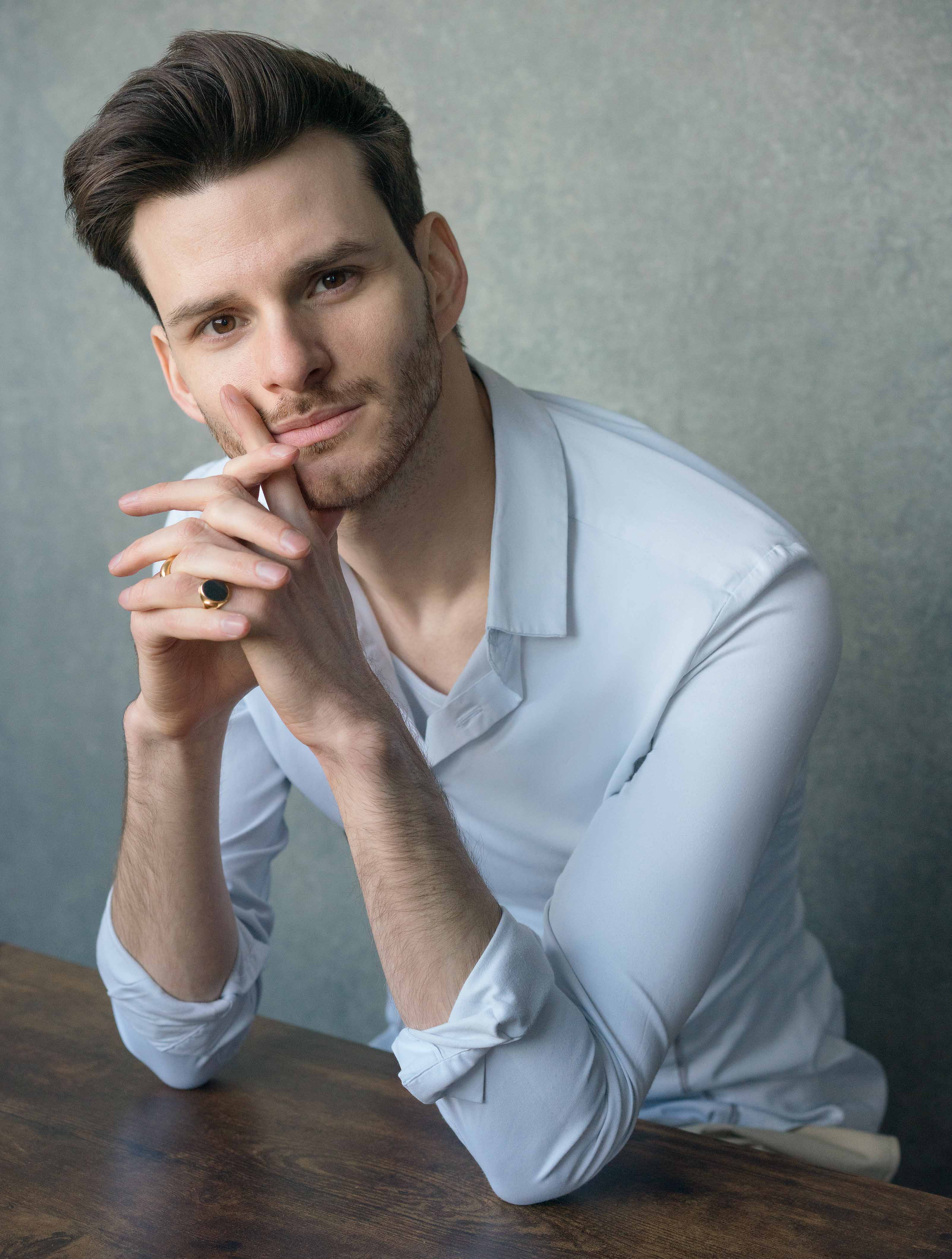 Sam Hume sits in a white shirt, leaning on a table, head resting gently in hands